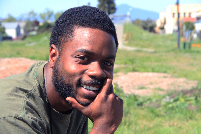 A smiling Black man with his hand on his chin.