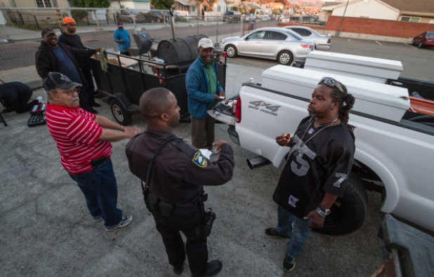 Officer Brandon Ruffin chats with a group of locals barbecuing in the Veteran’s Memorial Hall parking lot.  (Photo by Martin Totland, courtesy of Richmond Confidential)