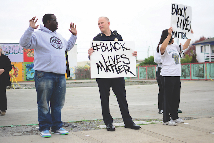 White police officer holding Black Lives Matter sign and looking at Black man
