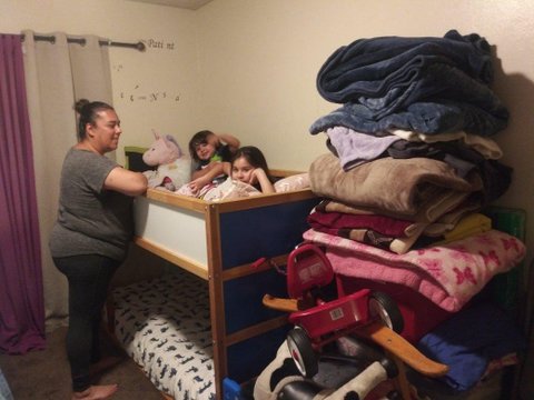 A woman stands next to her two small kids in the top of a bunk bed.