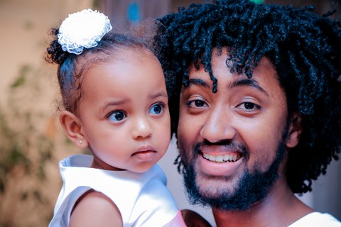 A smiling Black man holding a little girl with a flower in her hair.