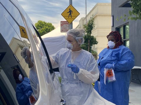 Coronavirus testers in mask, gowns, gloves and other protective equipment next to a car