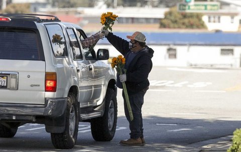 A man in a mask hands a bouquet of flowers to someone in a car.