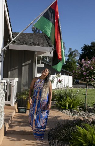 A Black woman in dress and braids looks up at a red, black and green flag.