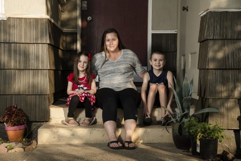 Woman sitting between her 5-year-old daughter and 7-year-old son on the steps in front of their house.