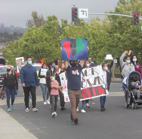 Adults and children in medical face masks march down a Richmond street.