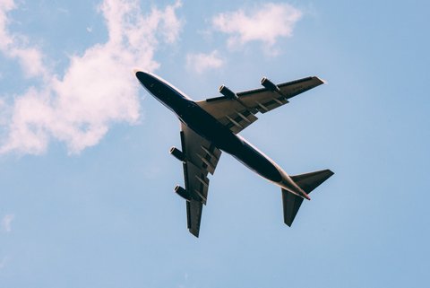 Airplane in flight, seen from below, against blue sky with sparse white clouds.