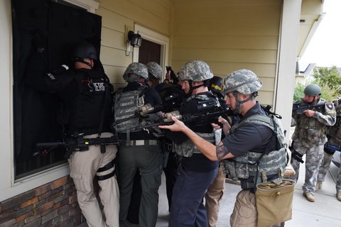 Trainee officers in SWAT gear in front of a house.