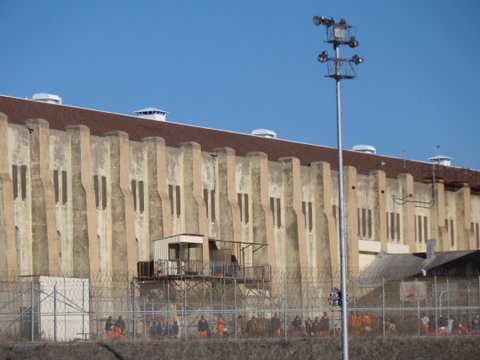 Exterior of San Quentin prison with convicts in orange seen through fence.