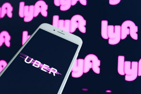 A smartphone with the word "UBER" on the screen and a backdrop with the word "lyft" repeated.
