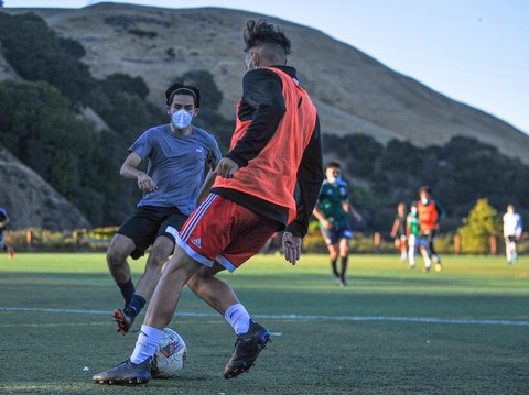 Two players in medical face masks go for the ball during a soccer tryout.