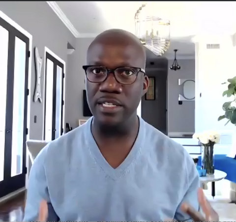 A Black man in a light blue V-neck and glasses.