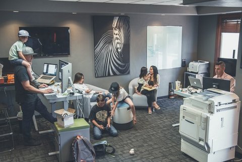 Adults and children in office with computers, copier and a photo of a zebra on the wall.