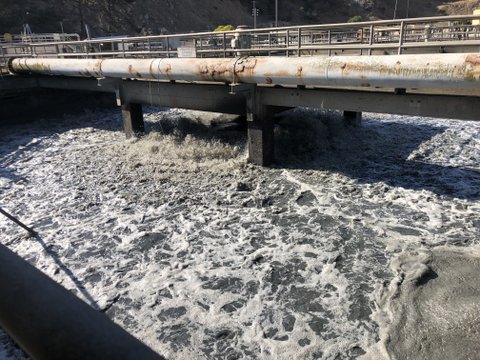 Churning water under a walkway with a rust-stained pipe next to it.