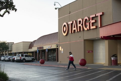 Person in face mask and red and white shirt walking away from a Target in a shopping center.