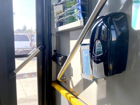 Dispensers for hand sanitizer and masks near back door of a bus.