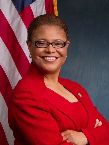A smiling Black woman in a red suit standing in front of the U.S. flag.