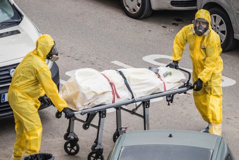 Two people in head-to-toe yellow protective gear with a covered body on a gurney.