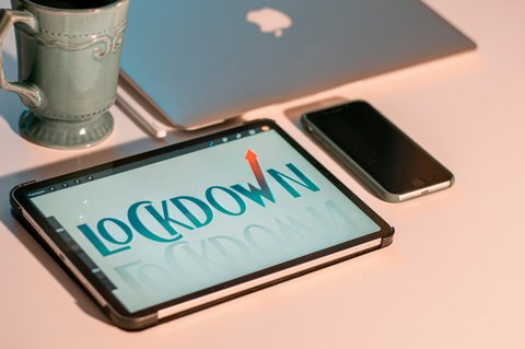 A tablet with the word "lockdown" on the screen next to a smartphone, MacBook and coffee mug.