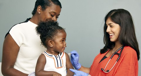 Woman in scrubs prepares toddler's arm for a shot with woman standing by.