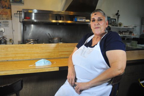 Woman in hairnet and apron sitting at counter with kitchen behind her and face mask next to her