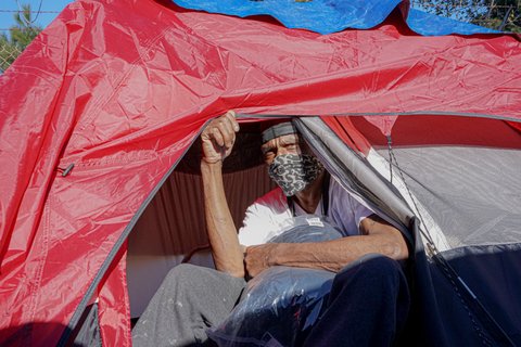 Man in face mask looks out of tent