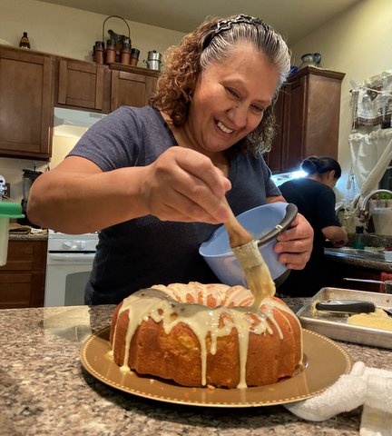 Smiling woman ices a bundt cake in her kitchen