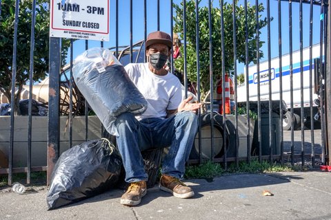 Sitting man in face mask holds wrapped sleeping bag