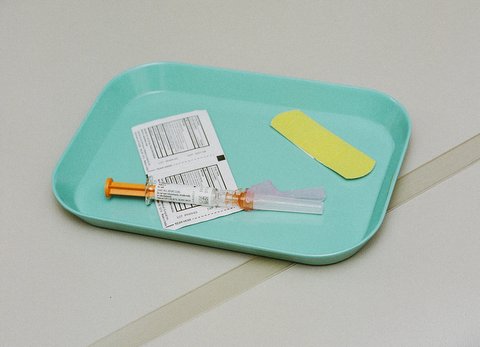 Vaccine syringe on tray with swabs and yellow bandage