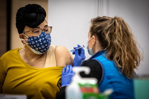Black woman in glasses and two masks gets vaccine shot.