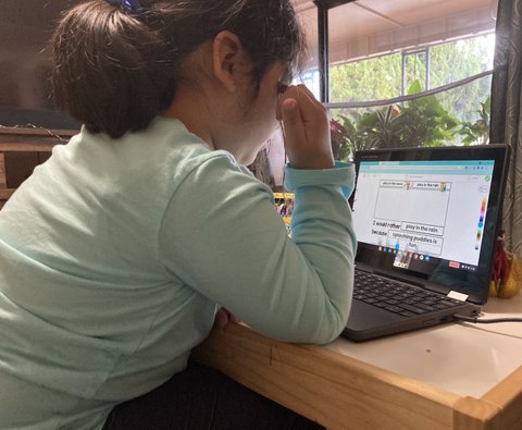 Side view of little girl looking at a laptop with her elbow propped on the table.