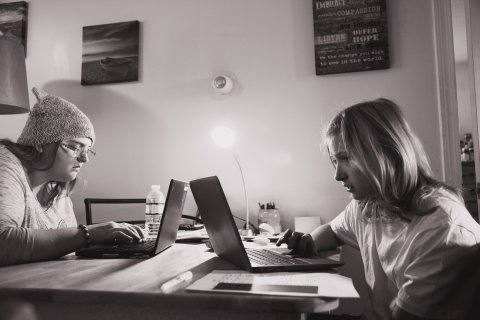 Black-and-white photo of a teen girl and a younger girl on laptops at a table.