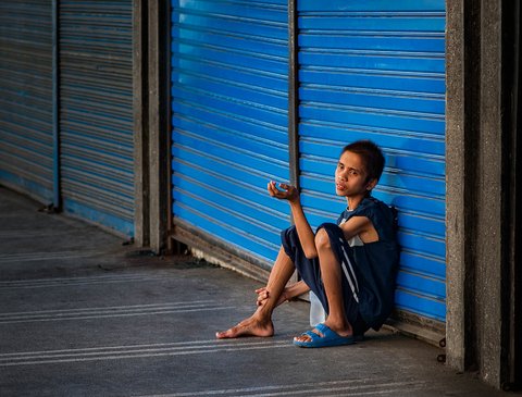 A malnourished young man sits with hand outstretched.