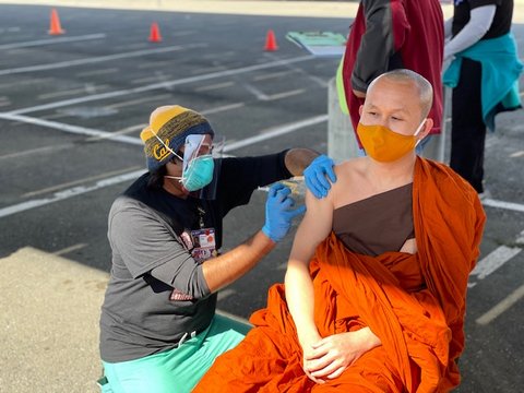 Man vaccinates man in orange Buddhist robes in parking lot