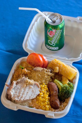 Brazilian food in open takeout box with green can of soda