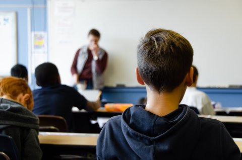 View from behind of a boy in a classroom looking toward an out of focus teacher