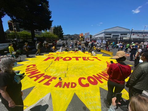 Street art of a yellow sun with the words "We are here to protect climate and community" in red.