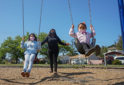 Latina woman pushing her two daughters on swings