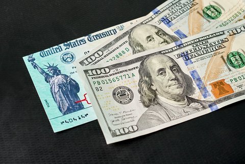 Two $100 bills partially covering a U.S. Treasury check