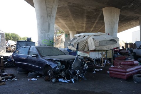 A car with a smashed front, an RV covered with canvas and debris under an overpass