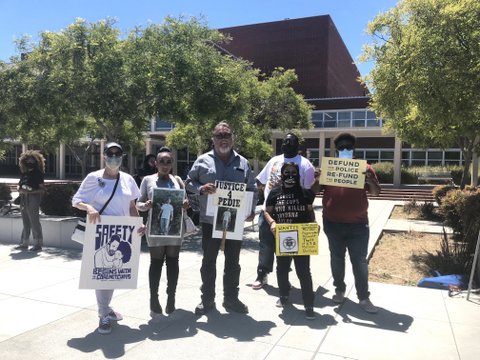 Five people holding signs with phrases like "Justice 4 Pedie," "Defund the police, refund the people" and "Safety begins with care not cuffs"