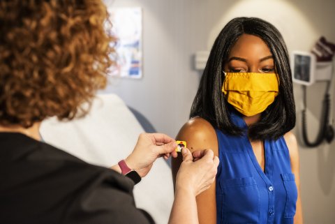 Black woman in blue top and yellow mask in doctor's office