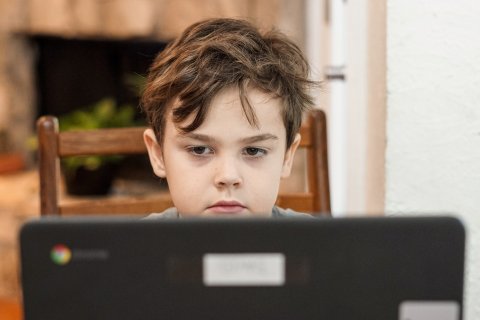 Young boy with unhappy expression seen over the top of a laptop screen.