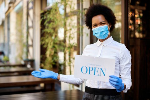 Black woman in mask and gloves holding open sign