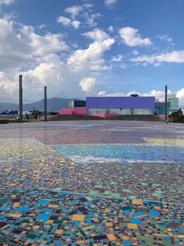 Ground with colorful patterns leading to pink and purple buildings with blue sky overhead