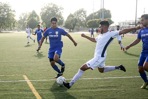 Soccer player with arms outstretched and leg poised to kick on the field with two defenders nearby