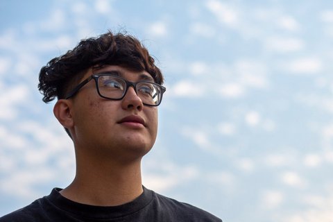 Young asian man looking off into the distance against a blue sky.