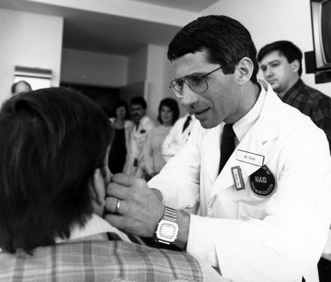 Black-and-white photo of a man in a lab coat examining a patient who is seen from behind.