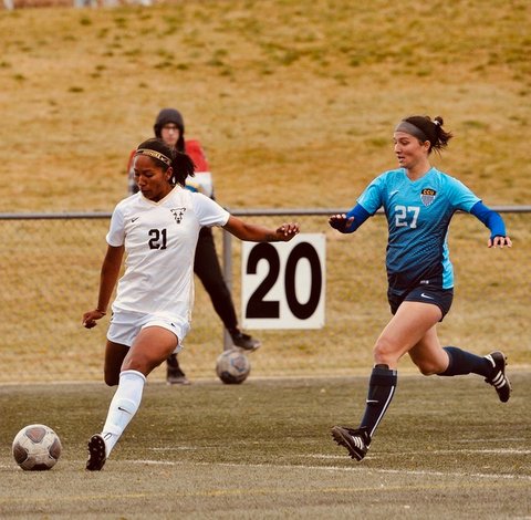 Soccer player in white moves the ball as an opponent in blue pursues her