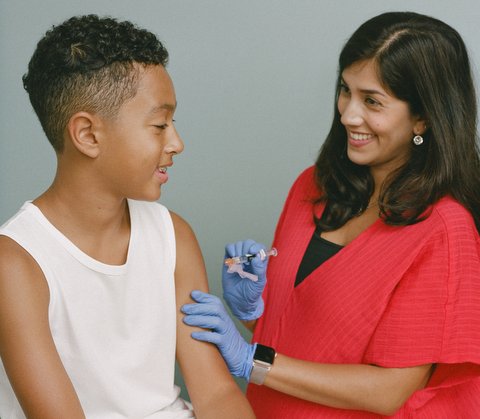 A boy and a smiling female medical professional holding a syringe